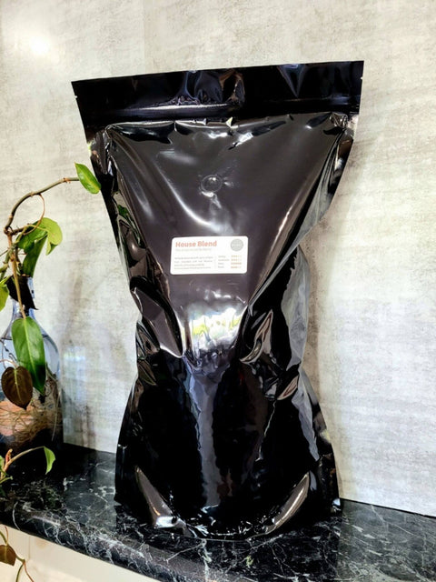 Sipping Duck 3kg bag of House Blend coffee in black with plants in the background.