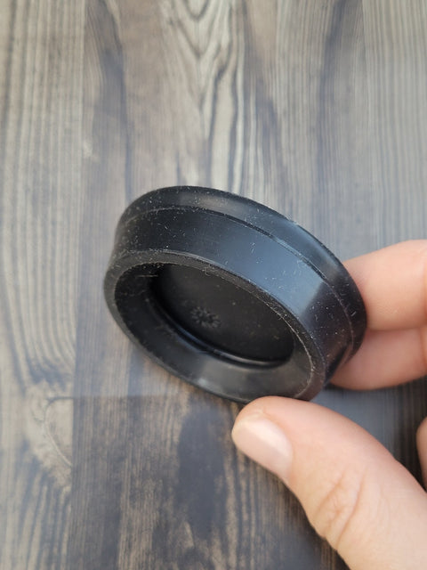 AeroPress plunger seal, black rubber, side view held by a hand on a wooden surface.
