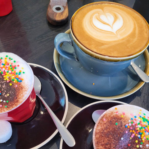 Latte in a mug and two babyccinos with marshmallows, chocolate sprinkles and colourful 100s & 1000s.