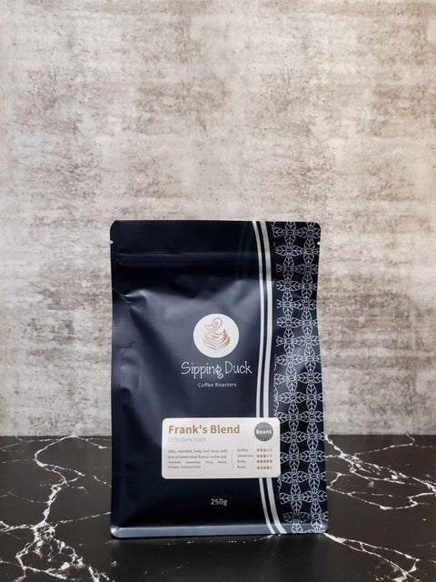 Sipping Duck Frank's Blend 25% dark roast coffee blend in blue coffee bag, label with profile description and unique pattern.