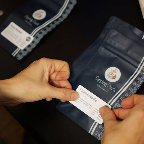 Sipping Duck Coffee Roasters bag being labelled by hand with Flight Mode sticker.