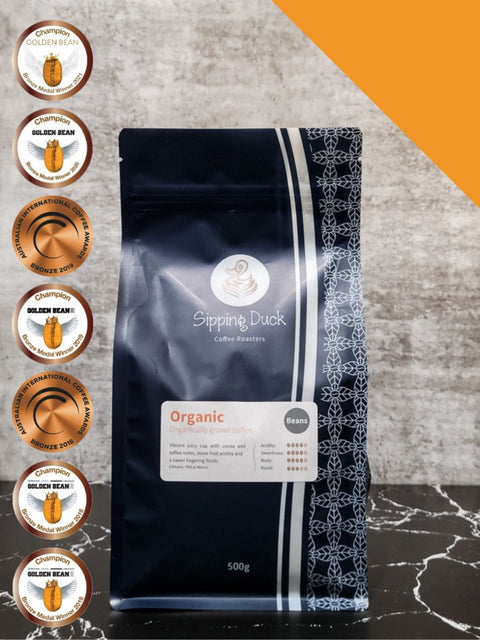 Sipping Duck Coffee Roasters Organic blend in blue bag with medals from Golden Bean and AICA coffee awards.