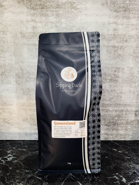 Sipping Duck Coffee Roasters Queensland specialty coffee in blue 1kg bag with unique pattern and label with blend description.