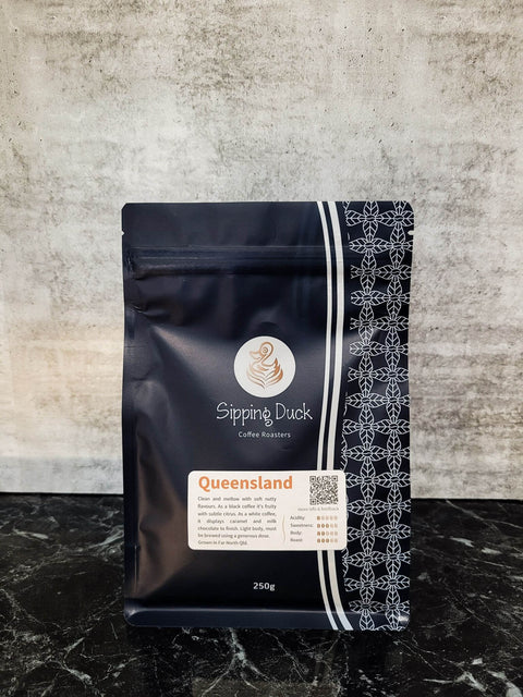 Sipping Duck Coffee Roasters Queensland specialty coffee in blue 250g bag with unique pattern and label with blend description.