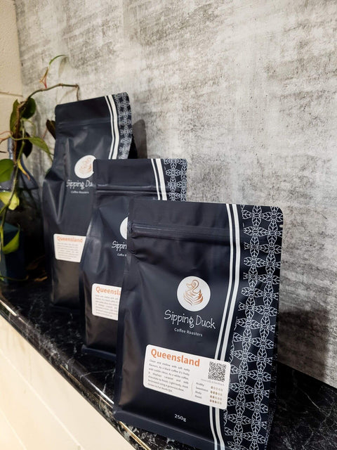 Sipping Duck Coffee Roasters Queensland specialty coffee in 3 sizes, blue bags with unique pattern and label with blend description.