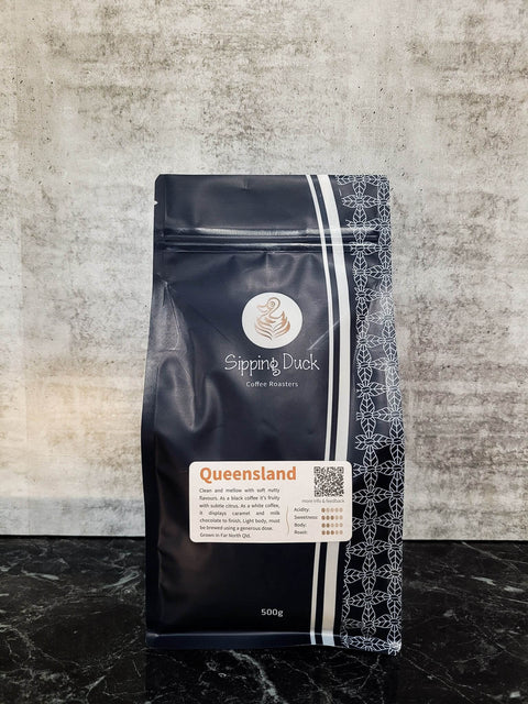 Sipping Duck Coffee Roasters Queensland specialty coffee in blue 500g bag with unique pattern and label with blend description.