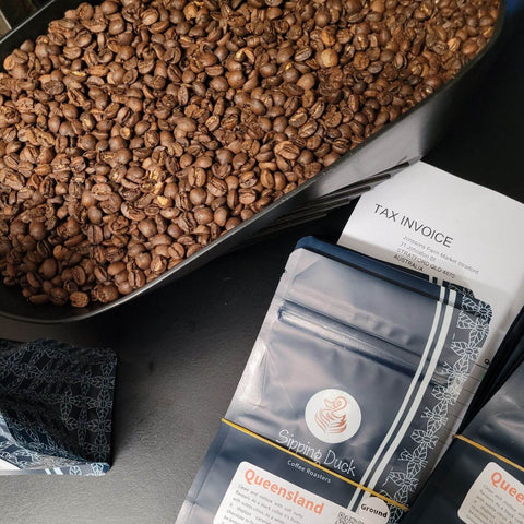 Sipping Duck Queensland coffee bags, tax invoice for Monsoons Farm Market and coffee beans in scoop.