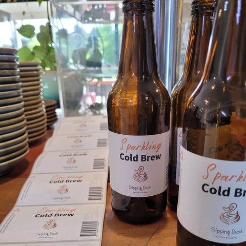 Sipping Duck Sparkling Cold Brew coffee bottles and labels with plant and saucers in the background.