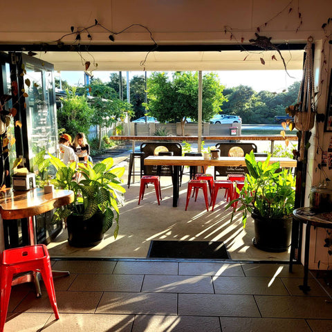 Sipping Duck Stratford Cairns cafe in the morning light, open doors, plants, indoor and outdoor seating, cars and trees in the background.